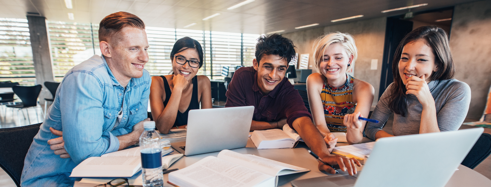 Five students sit around a table with two computers